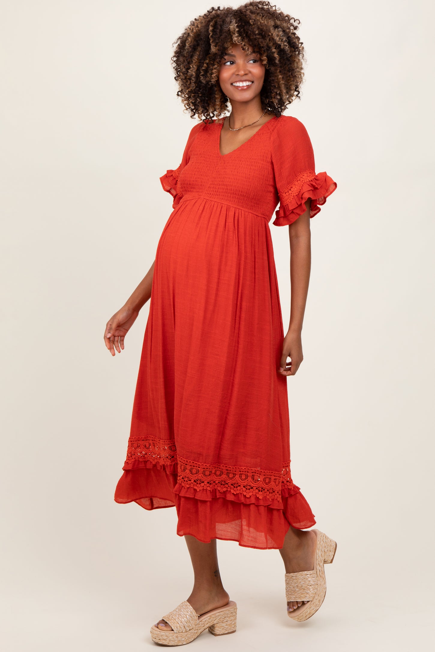 woman wearing an orange maternity dress with short ruffled sleeves and lace trim, showcasing her baby bump