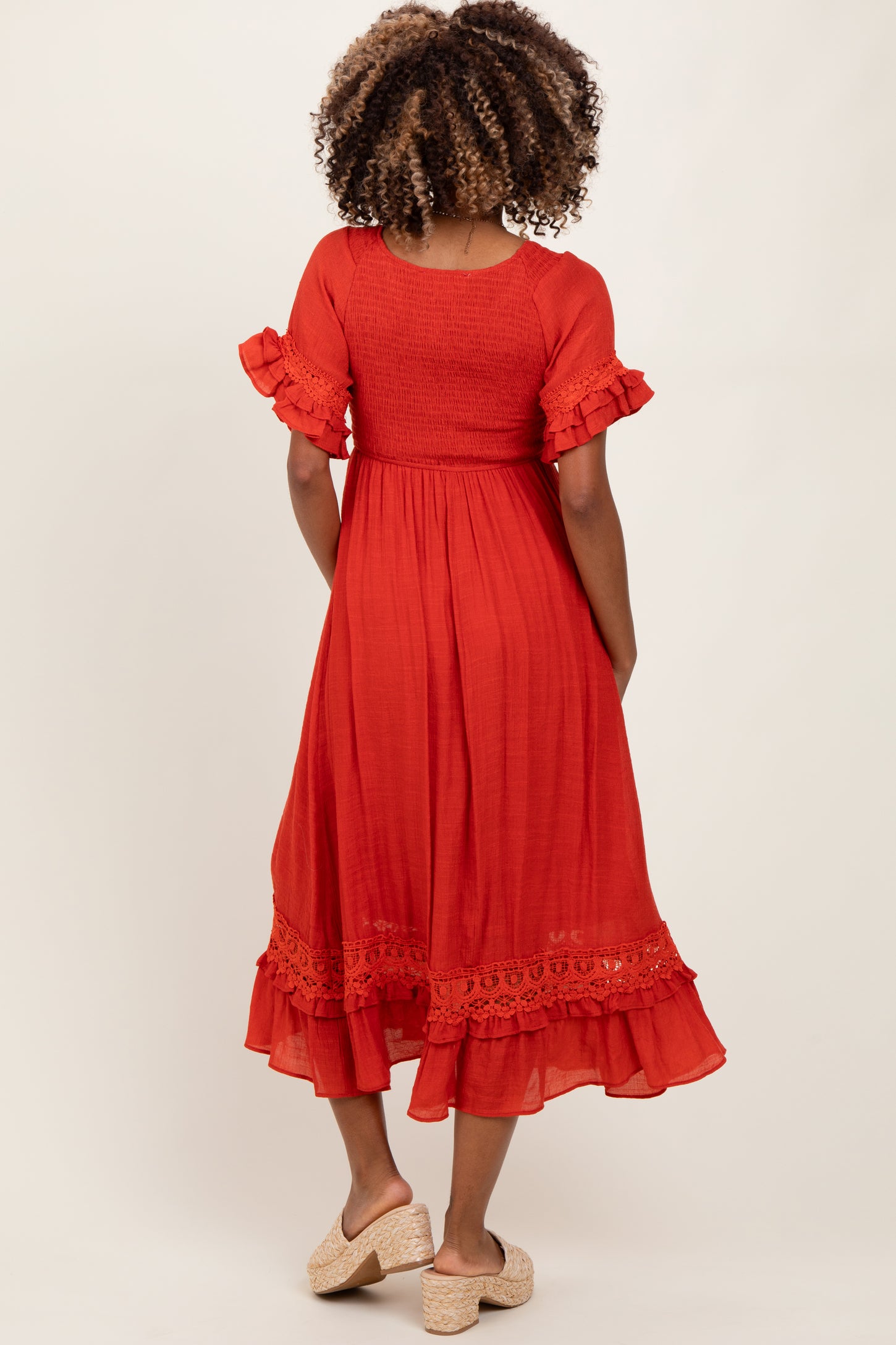 woman wearing a back view of a red maternity dress with ruffle sleeves and a lace trim at the hem
