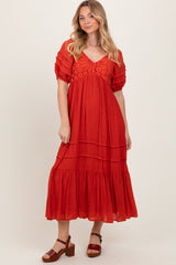 woman wearing a rust tiered maxi dress with short puff sleeves and lace detailing at the neckline