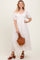 woman wearing a white maxi dress with lace detailing, holding a brown handbag and wearing brown heeled sandals