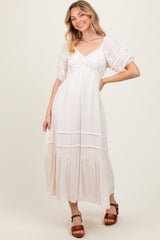 woman wearing a white maxi dress with lace details and puff sleeves, smiling and posing against a beige background