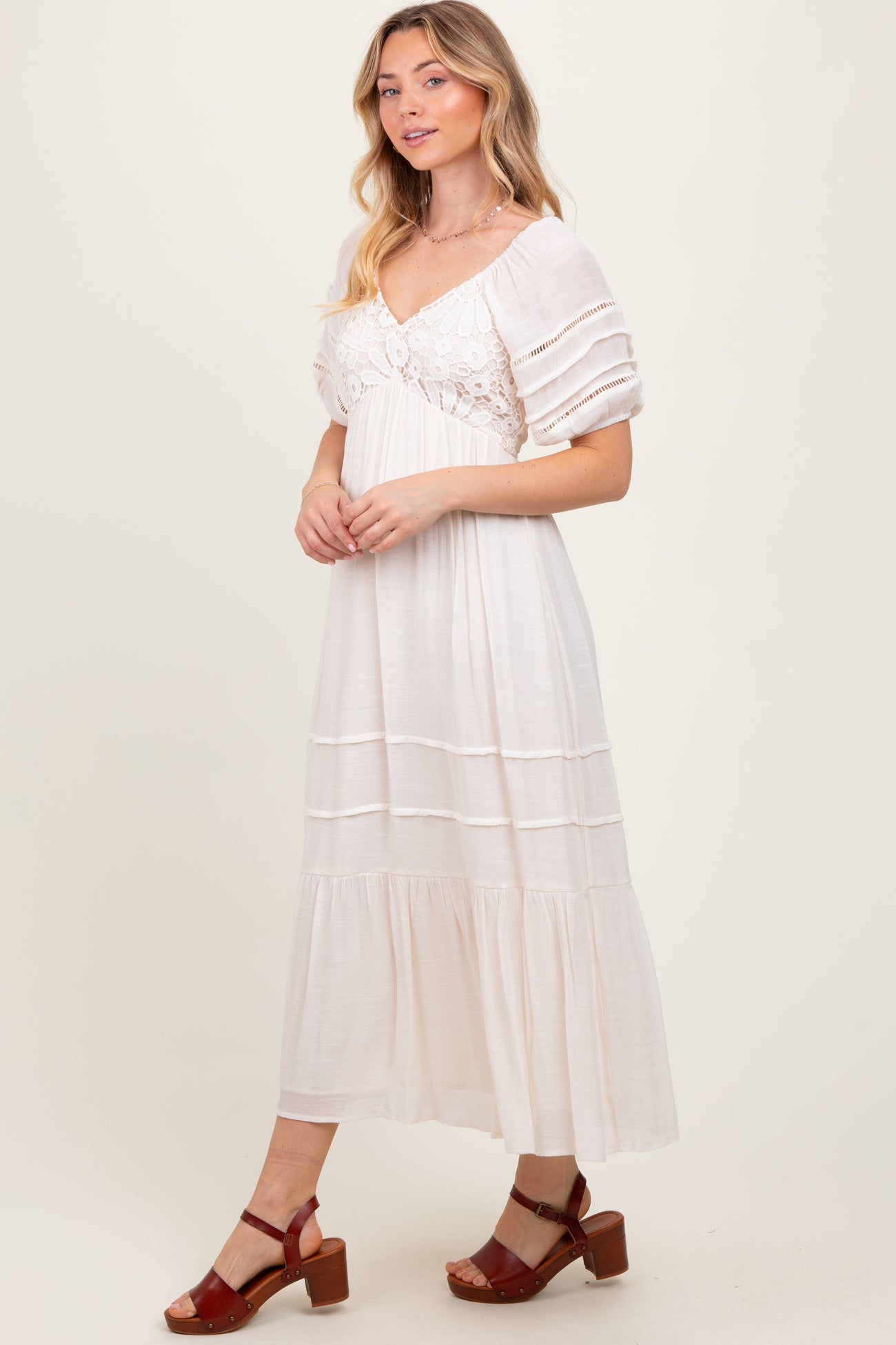 woman wearing a white maxi dress with puff sleeves and lace detailing, standing and smiling