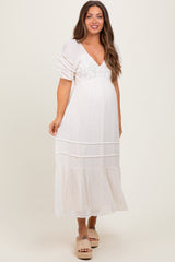 woman wearing a white maternity maxi dress with puff sleeves and lace details, showcasing her baby bump