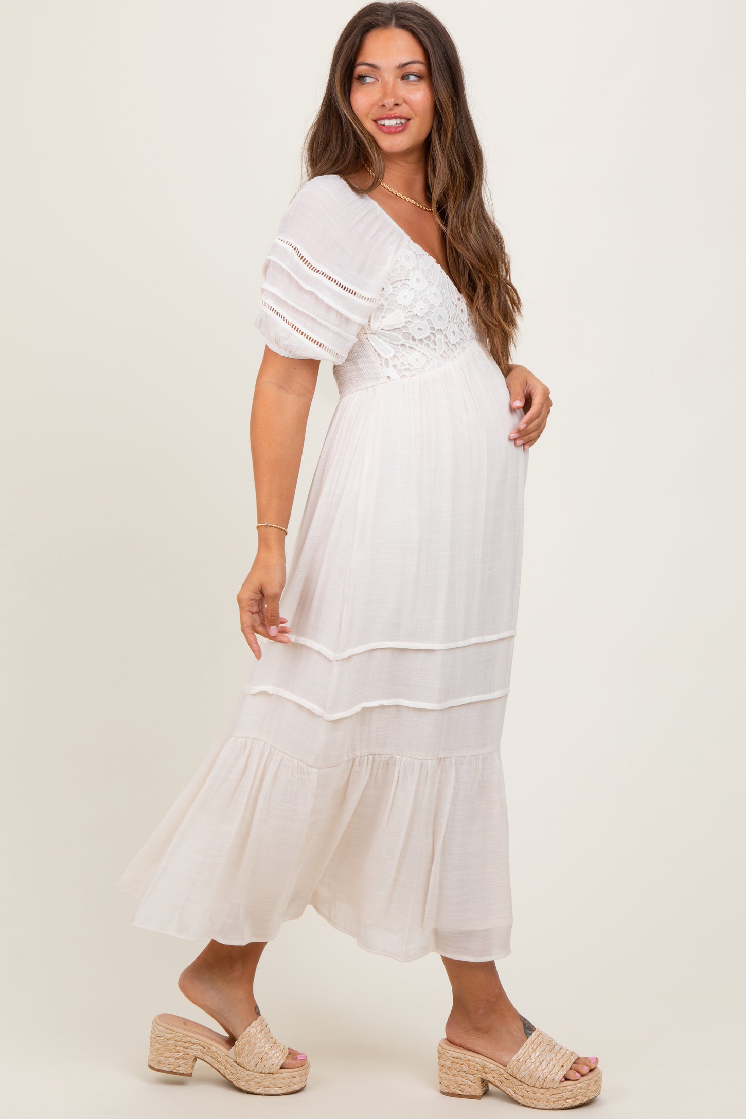 woman wearing a white maternity dress with puff sleeves and lace details, showing off her baby bump