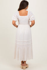 woman wearing a white maternity dress with puff sleeves and tiered skirt, seen from the back