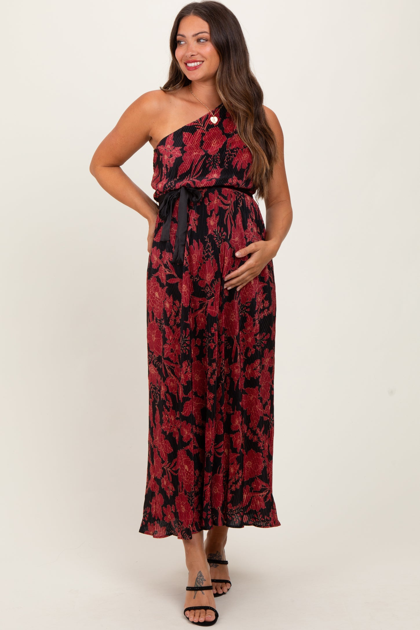 woman wearing a black and red floral one-shoulder maternity dress and holding her baby bump