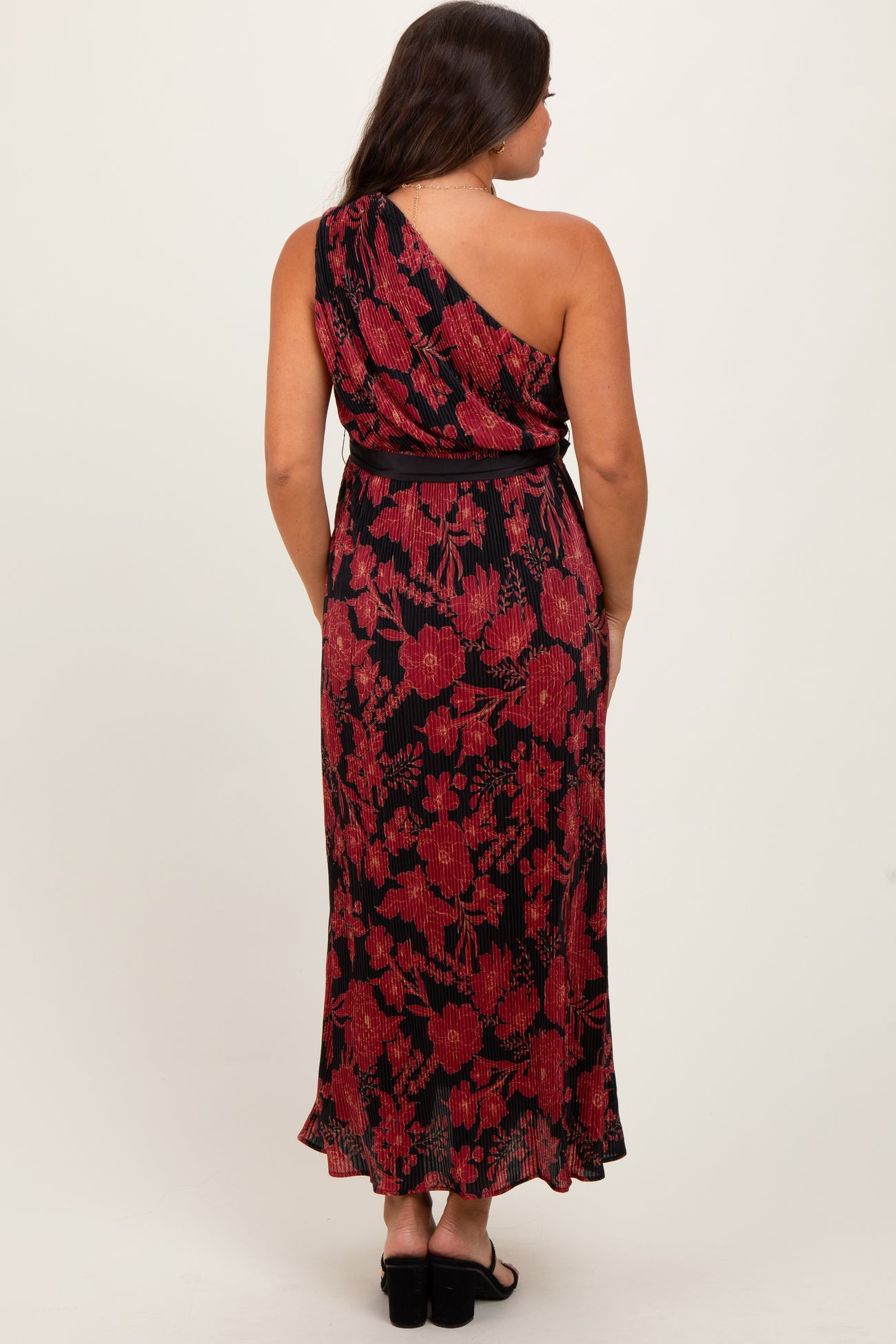 woman wearing a black and red floral maternity maxi dress with an asymmetrical neckline and tied waist