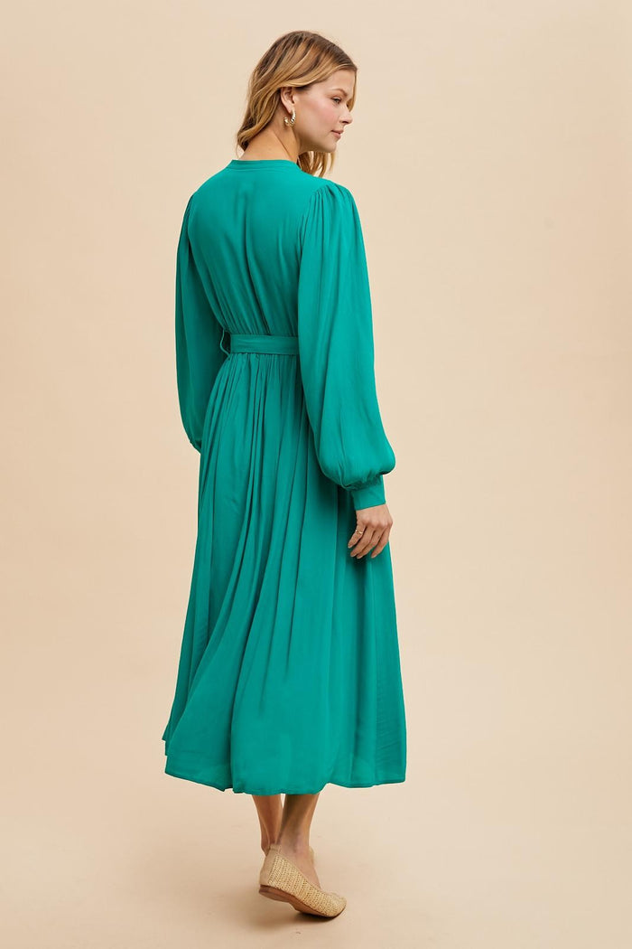 woman wearing a teal long sleeve maxi dress with a cinched waist and flowing skirt, viewed from the back