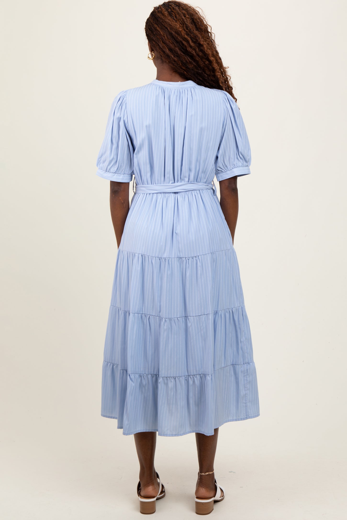 woman wearing a light blue tiered maxi dress with short puff sleeves and a cinched waist, shown from the back