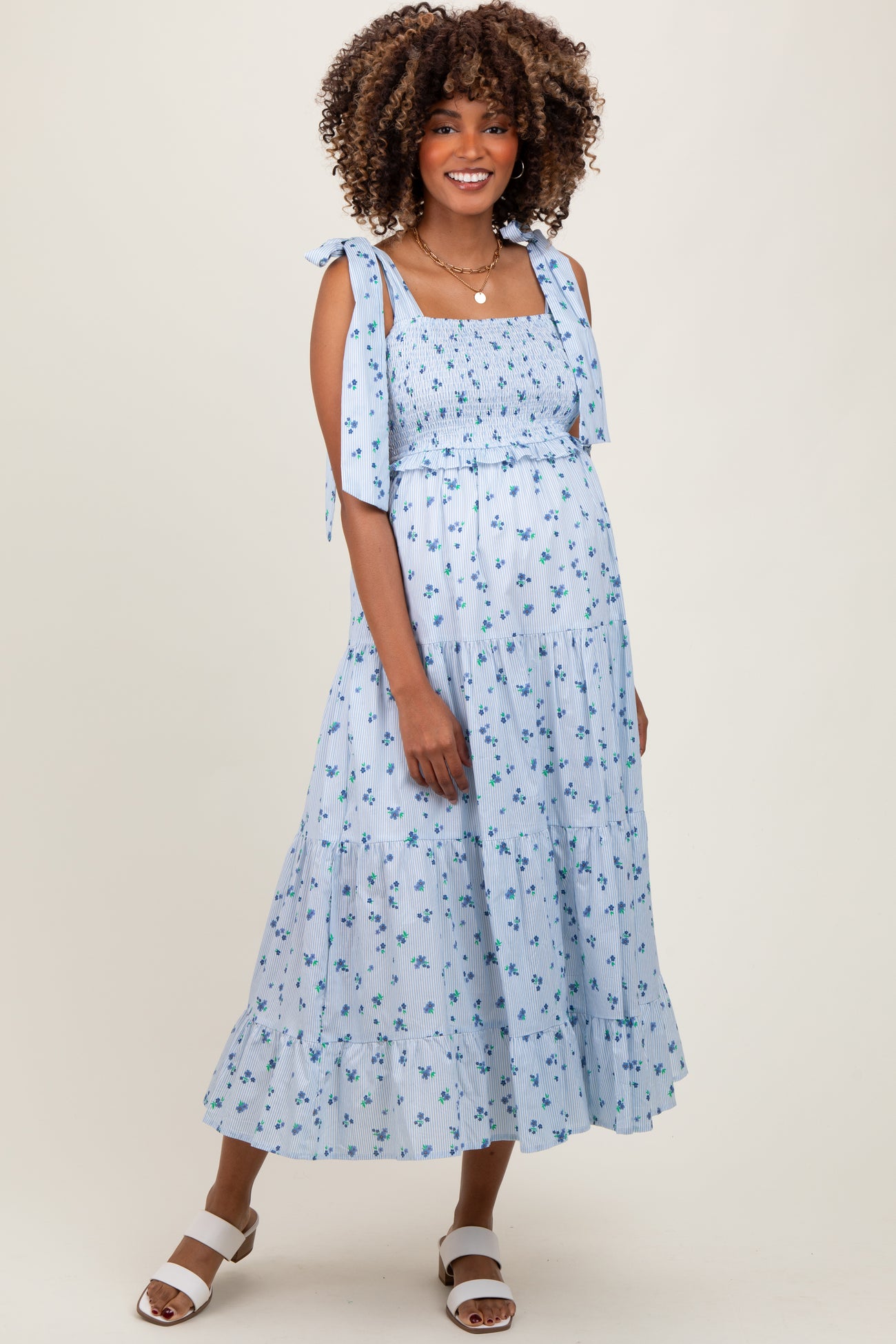 woman wearing a light blue maternity dress with floral print, smocked bodice, and tie straps, showing baby bump