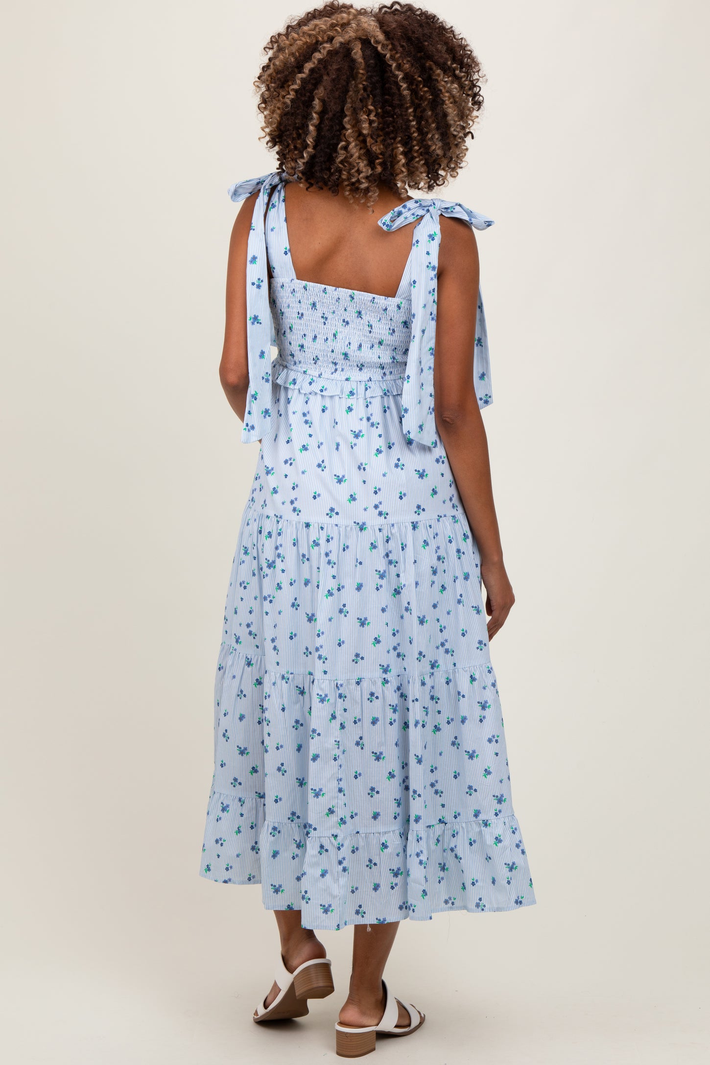 woman wearing a light blue maternity dress with floral print and tie straps, showing a relaxed fit and tiered skirt