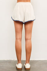 woman wearing cream-colored shorts with blue pom-pom trim and a relaxed fit