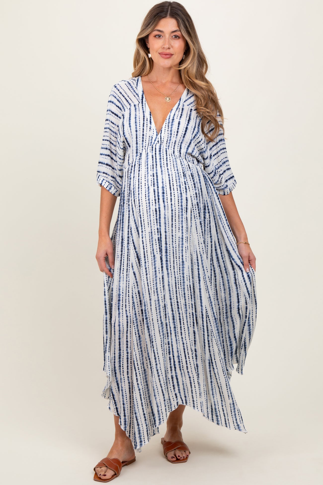 woman wearing a blue and white striped maternity maxi dress with a deep v-neckline and flowing sleeves, showing her baby bump