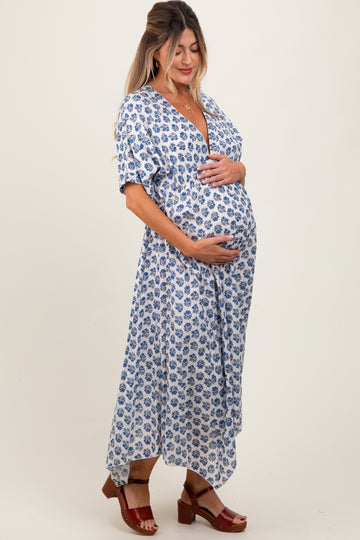 woman wearing a white floral maternity dress with short sleeves and a deep v-neck, gently cradling her baby bump