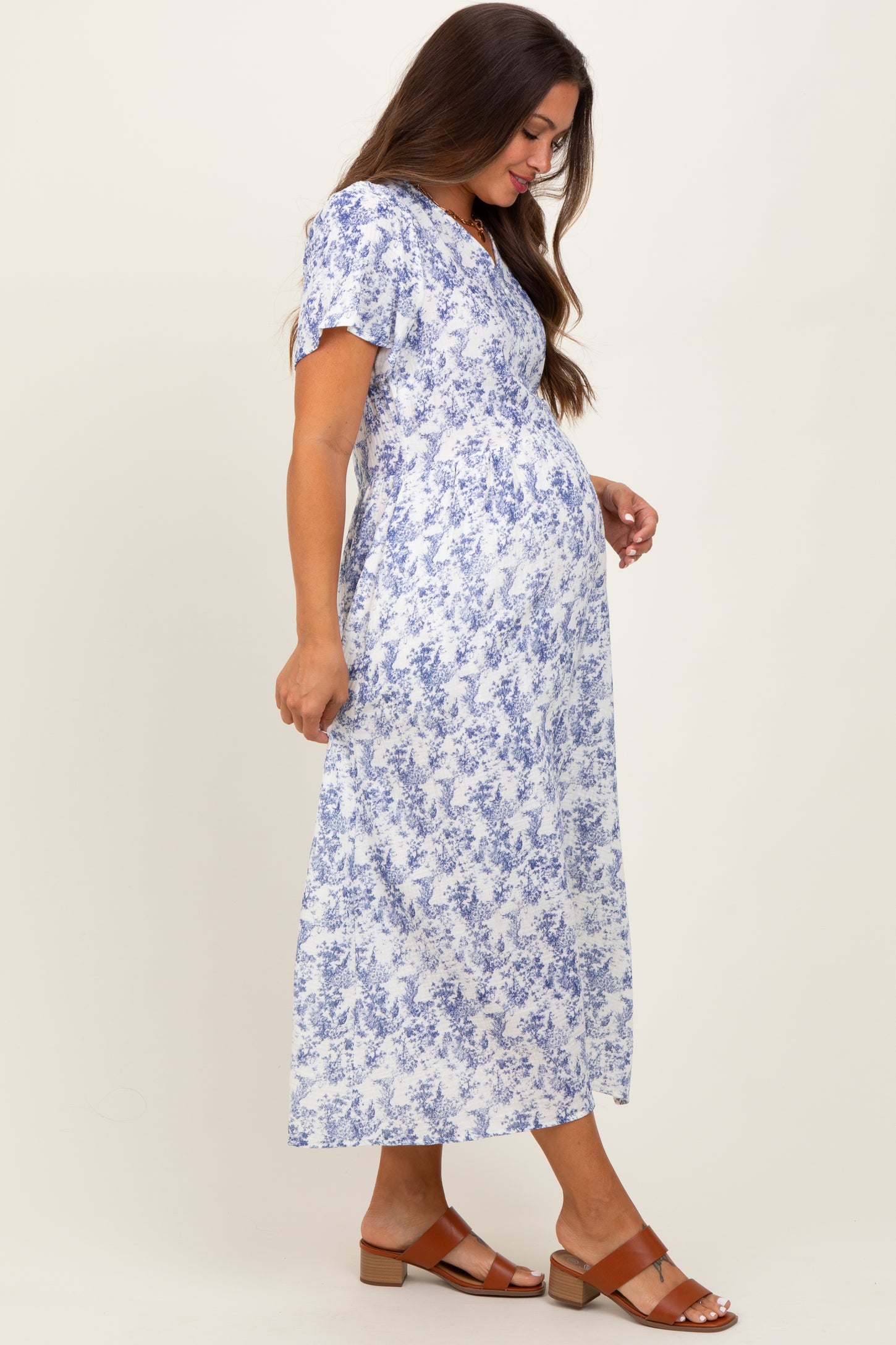 woman wearing a white floral maternity maxi dress with short sleeves and a visible baby bump
