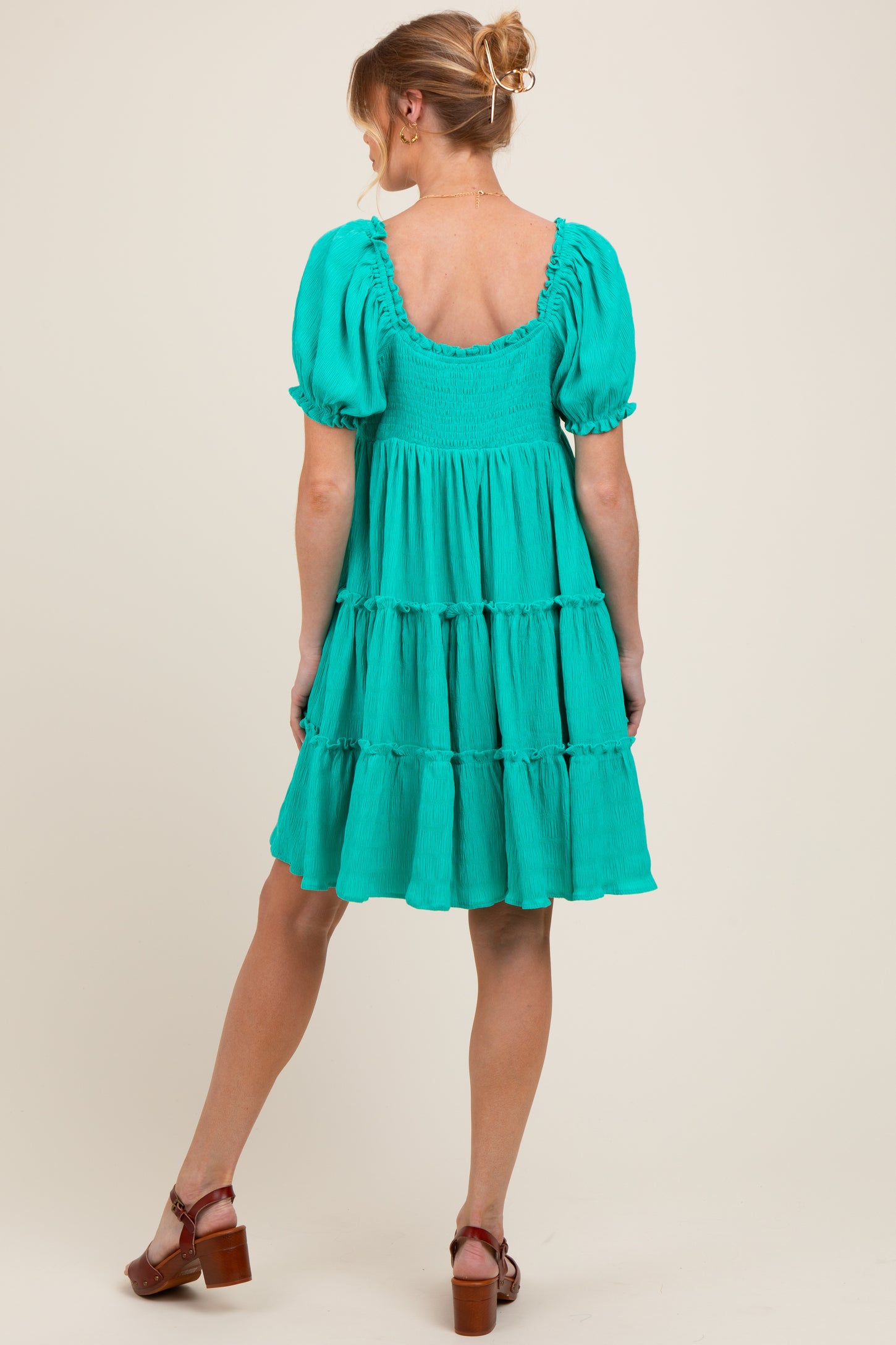woman wearing a teal maternity dress with puff sleeves and a tiered skirt, showing off her pregnant belly from the back