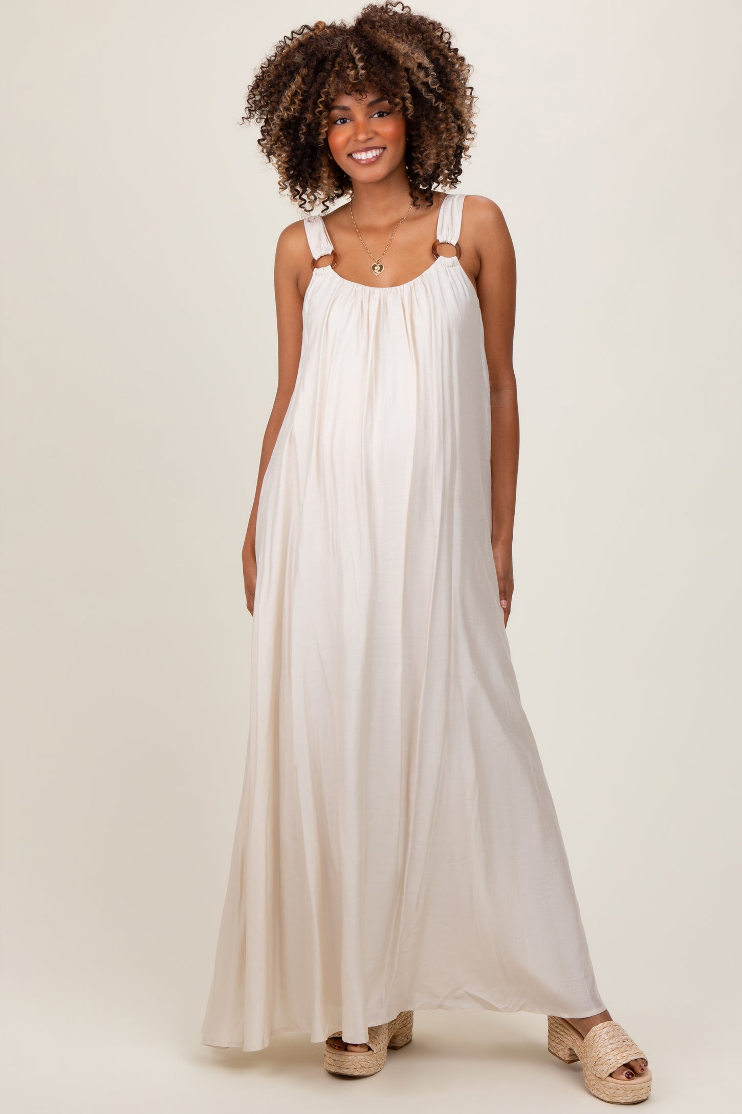 woman wearing a cream maxi maternity dress with adjustable straps and a flowing silhouette, showcasing her baby bump