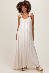 woman wearing a cream maxi maternity dress with adjustable straps and a flowing silhouette, showcasing her baby bump