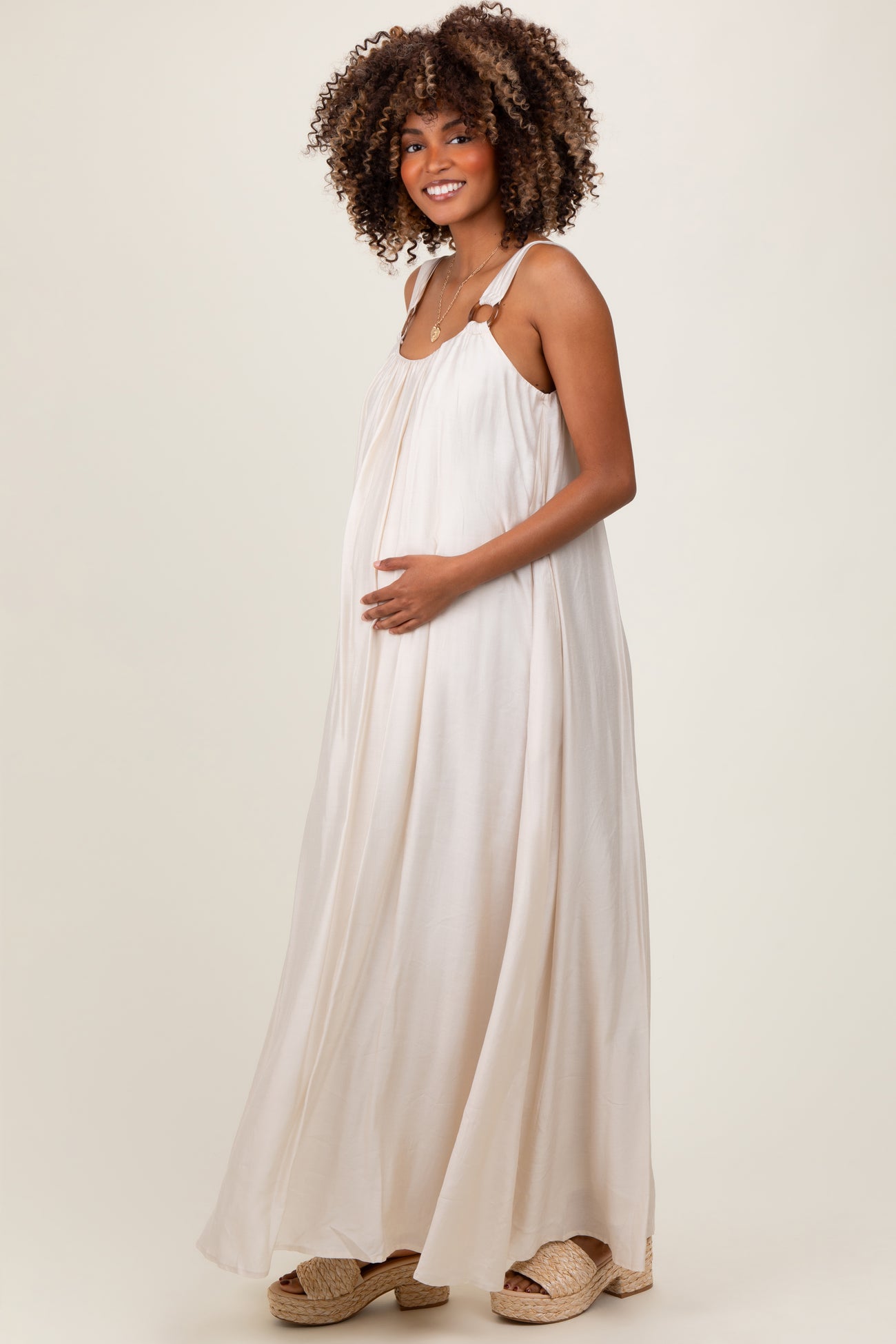 woman wearing a flowing cream maternity maxi dress and holding her baby bump