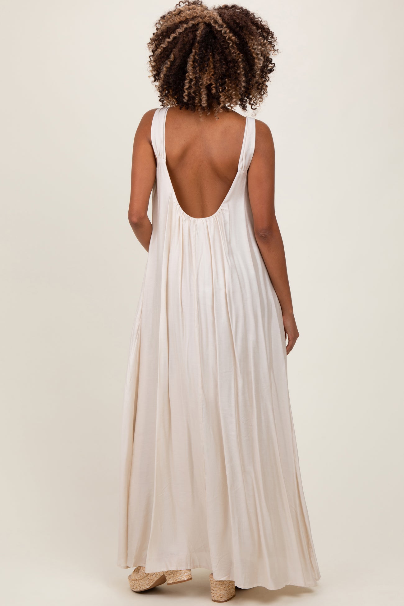 woman wearing a backless cream maternity maxi dress with a flowy silhouette and wide straps