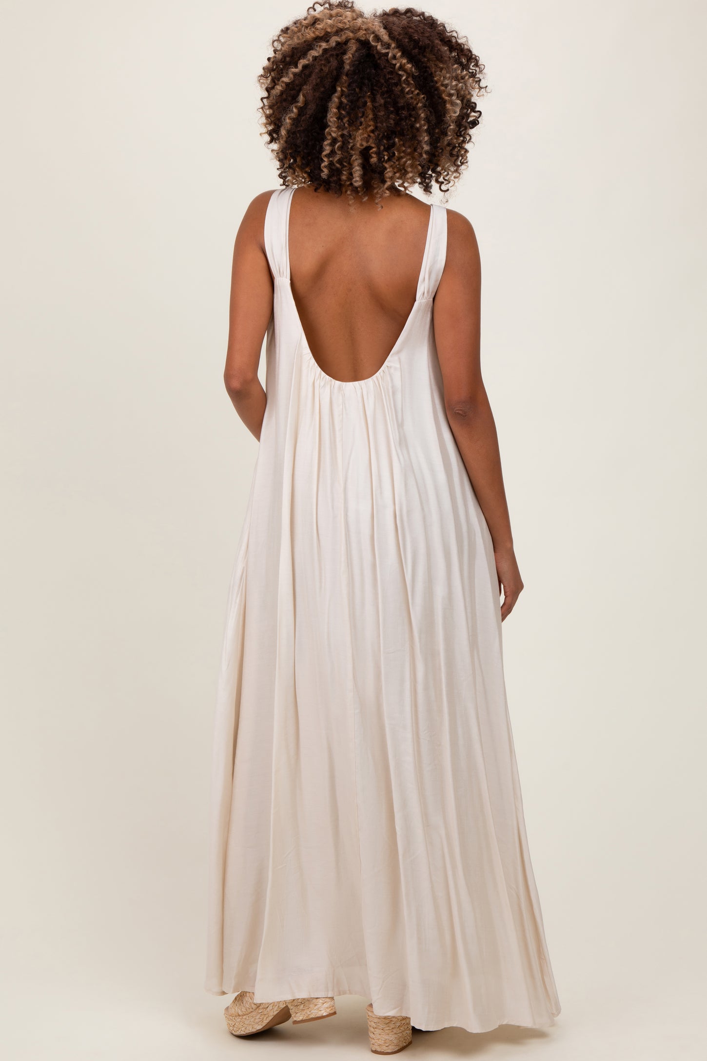 woman wearing a backless cream maternity maxi dress with a flowy silhouette and wide straps