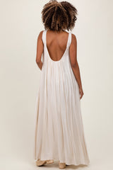 woman wearing a backless cream maternity maxi dress with a flowy silhouette and wide straps