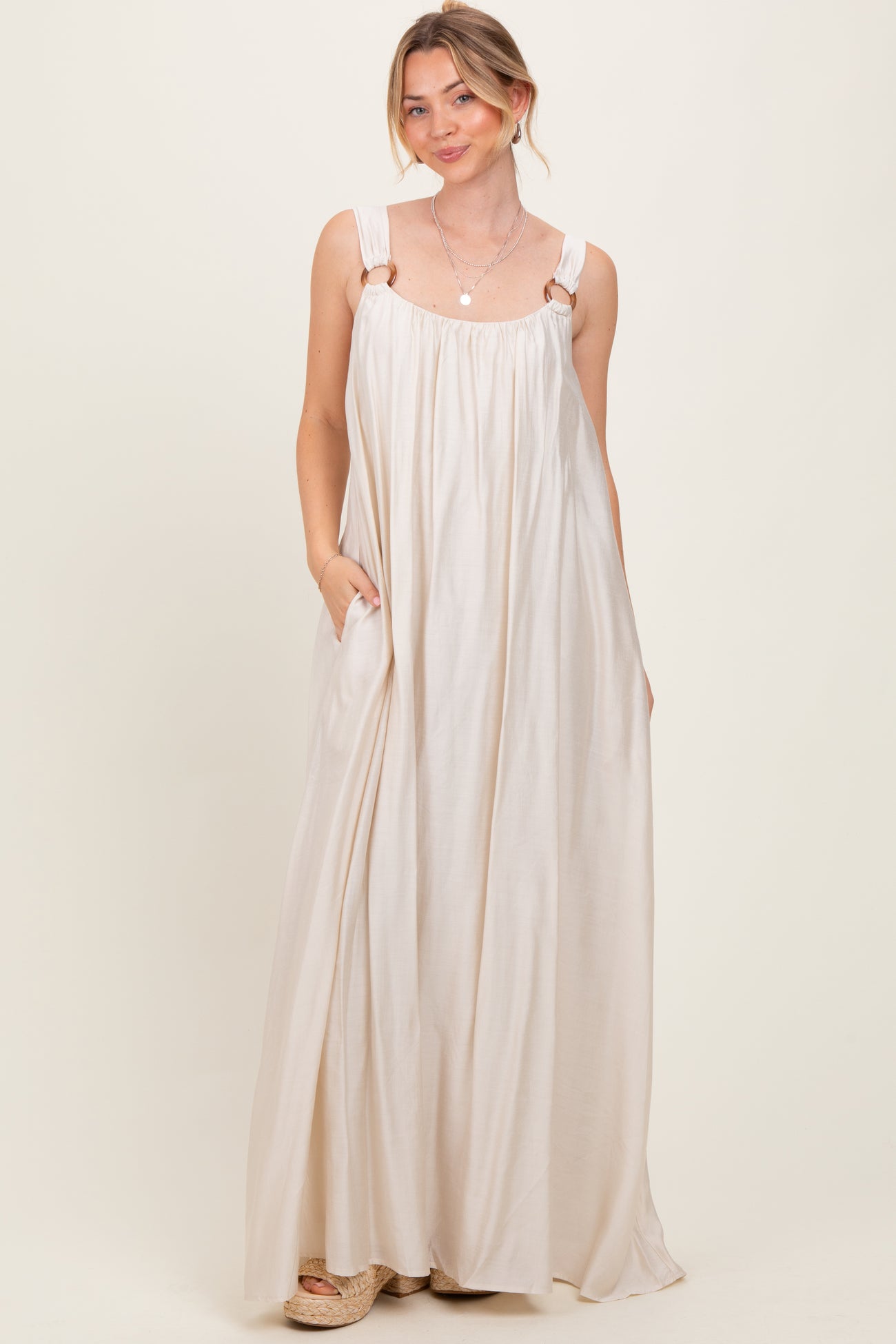 woman wearing a flowy cream maxi dress with adjustable straps and pockets