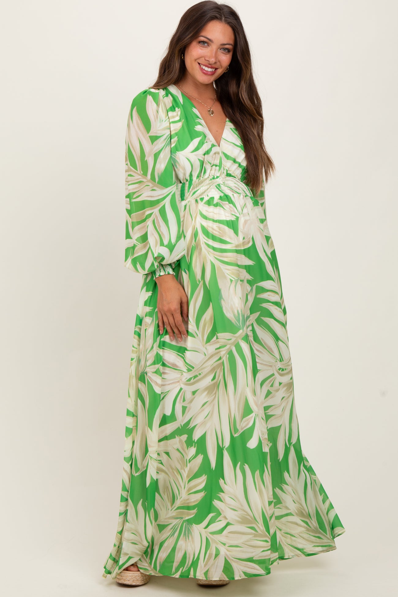 woman wearing a green floral print maternity maxi dress with long sleeves and a v-neckline, showcasing her baby bump