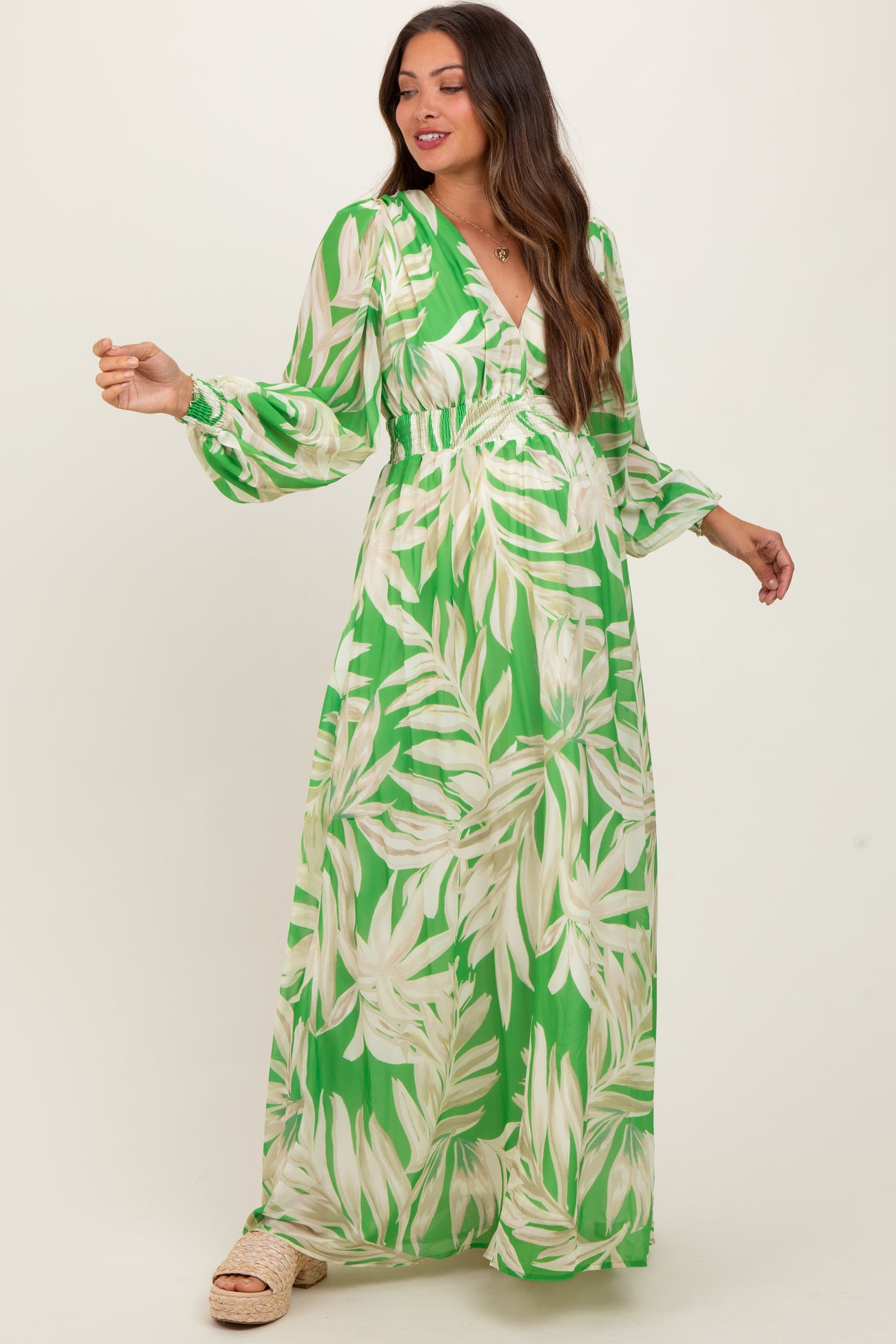 woman wearing a green maternity maxi dress with leaf print and long sleeves, showcasing her baby bump
