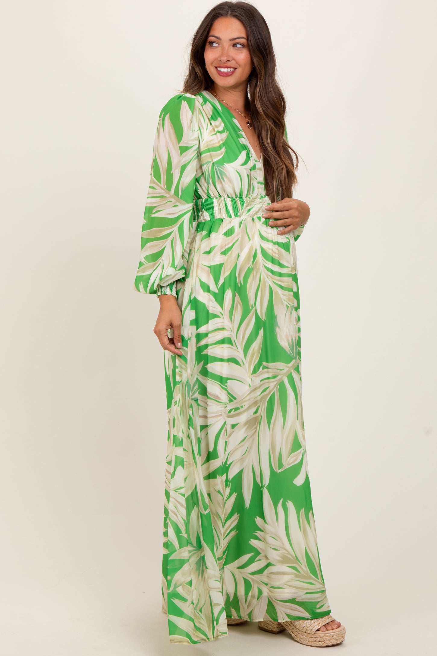 woman wearing a green maternity maxi dress with a leaf print and a baby bump visible
