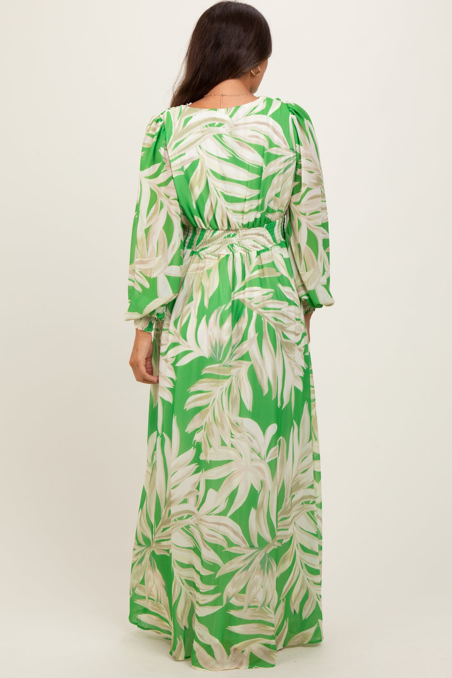 woman wearing a green tropical print maternity maxi dress with long sleeves and an elastic waist