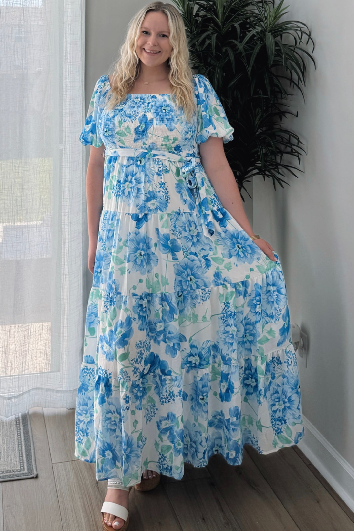 woman wearing a white maxi dress with blue floral print and puff sleeves, standing in a bright room