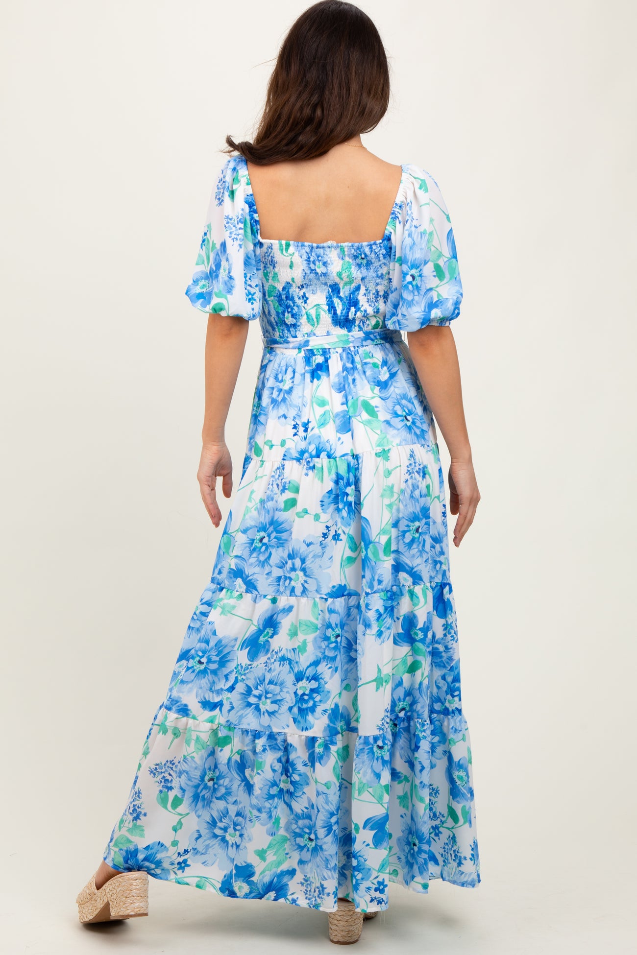 woman wearing a blue and white floral maxi dress with puff sleeves and a square neckline, back view