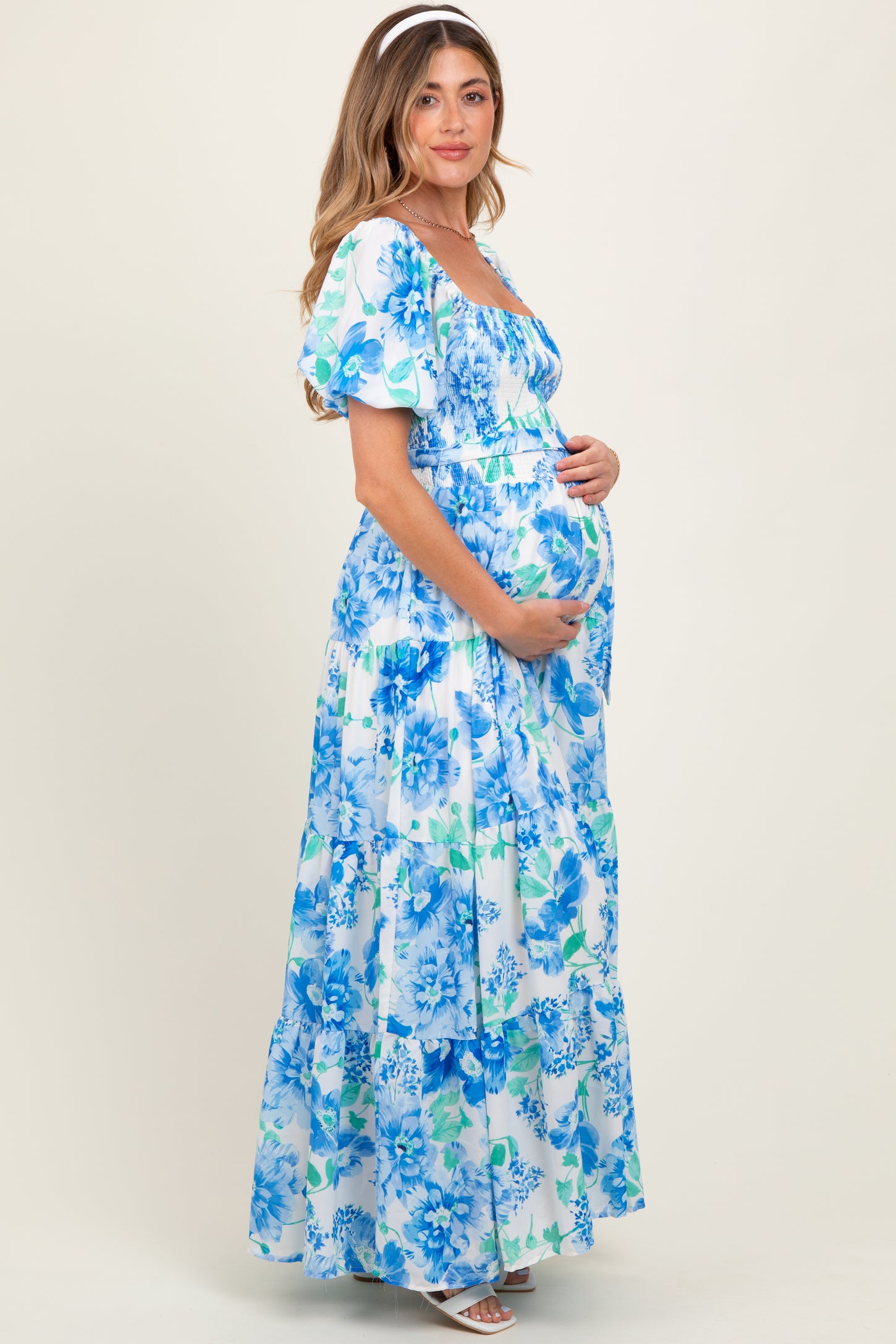 woman wearing a floral maternity maxi dress in blue and white, holding her baby bump