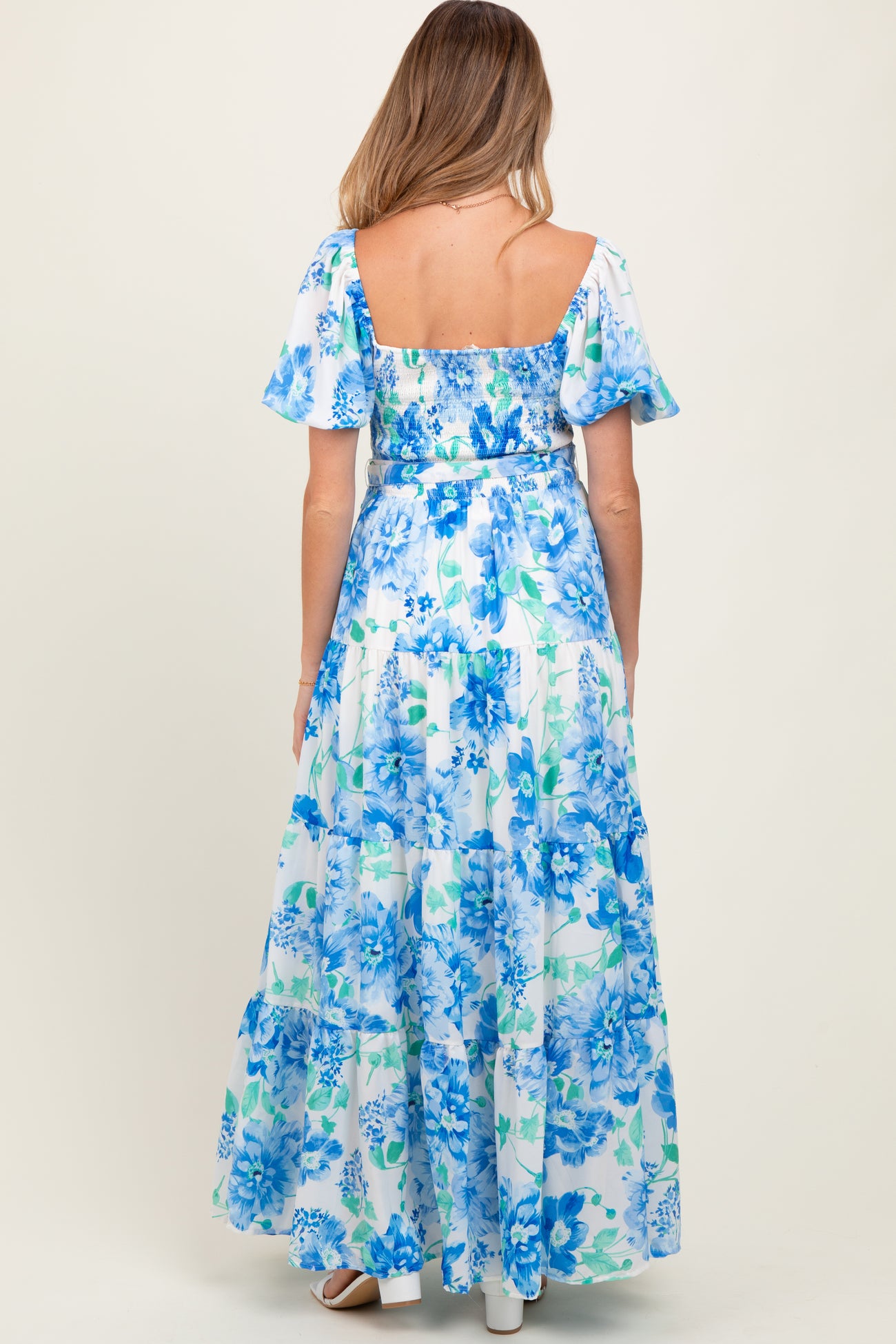 woman wearing a blue floral maternity maxi dress with short puff sleeves and a tiered skirt, showing her baby bump
