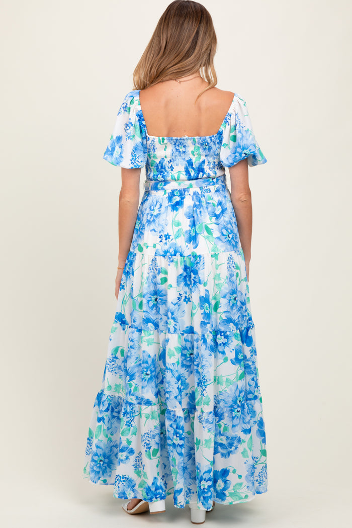 woman wearing a blue floral maternity maxi dress with short puff sleeves and a tiered skirt, showing her baby bump