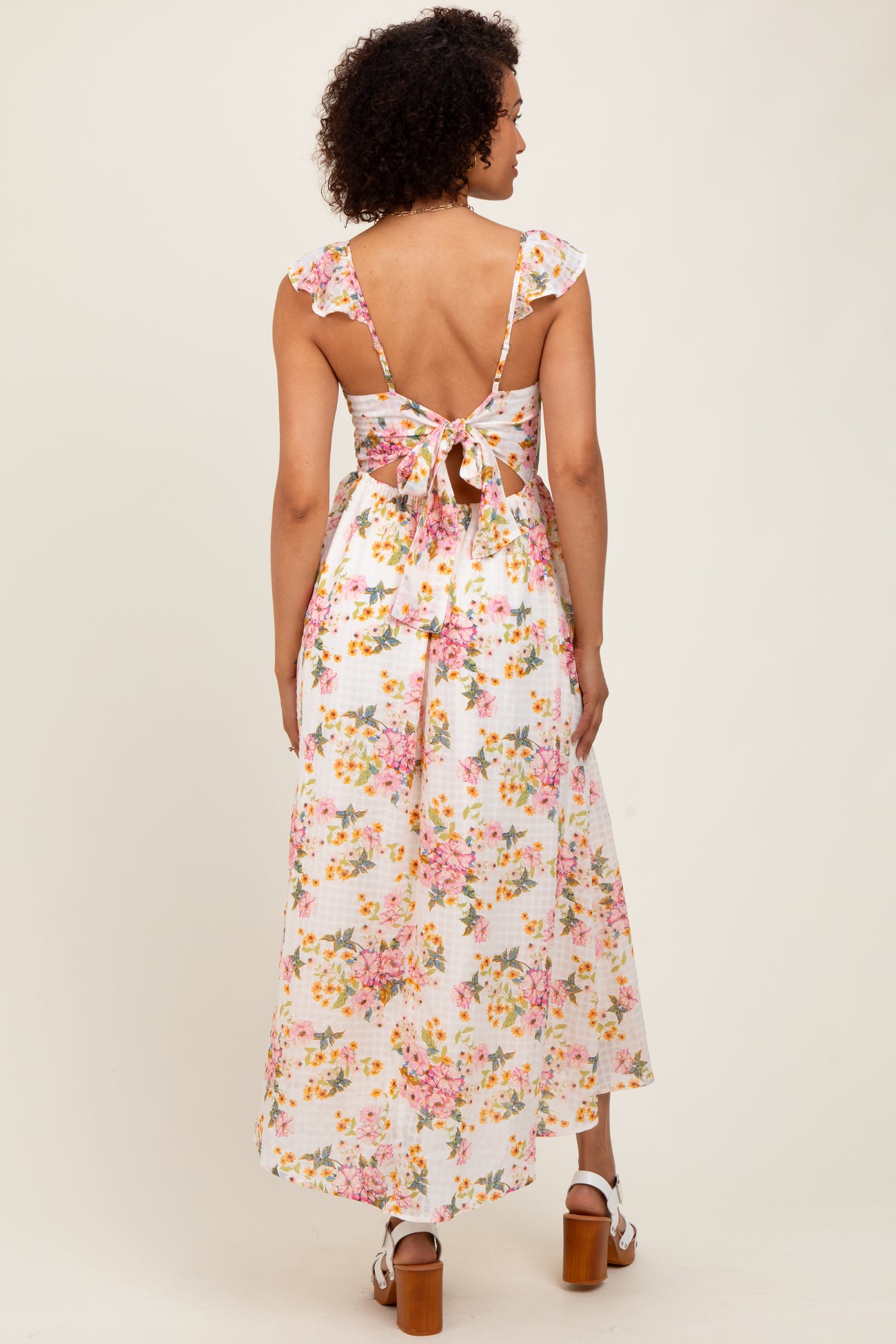 woman wearing a floral print backless maxi dress with ruffled straps and a tie at the waist