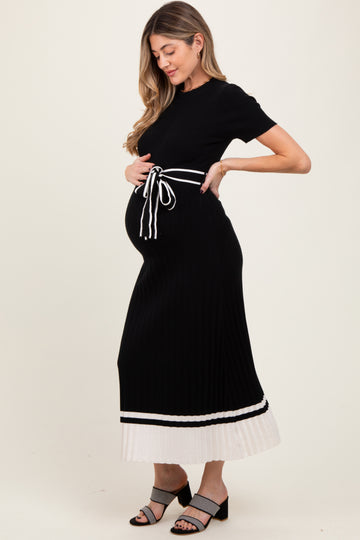 woman wearing a black maternity dress with a tie waist and white hem detail, holding her baby bump
