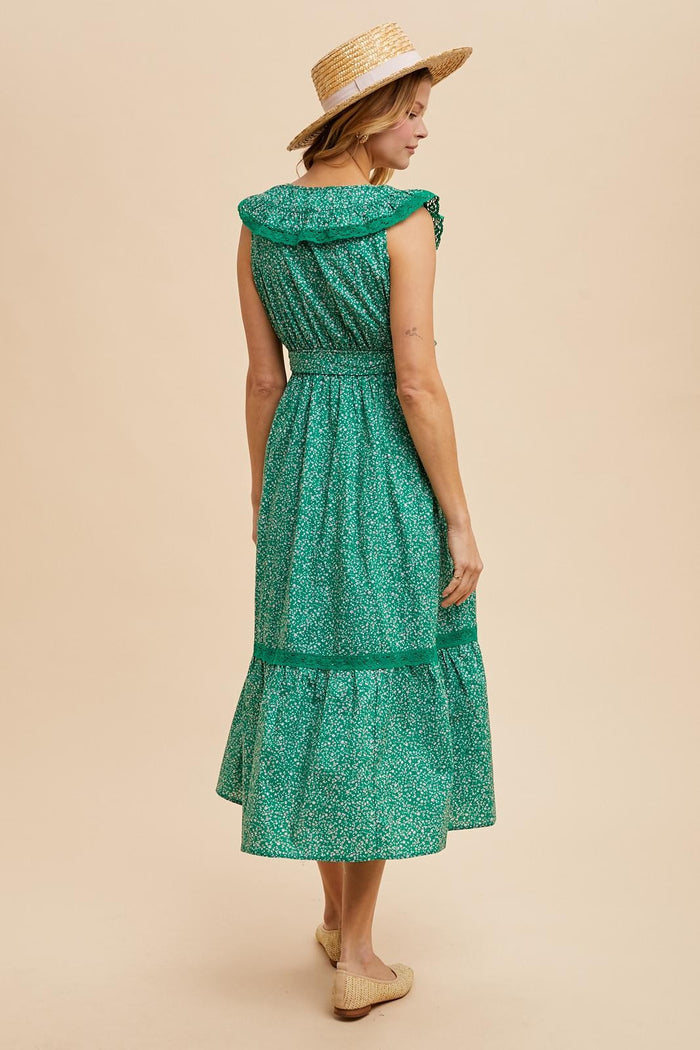 woman wearing a green floral midi dress with ruffled sleeves and a tiered skirt, accessorized with a straw hat
