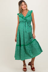 woman wearing a green floral maternity dress with ruffled sleeves and a tie waist, standing and smiling