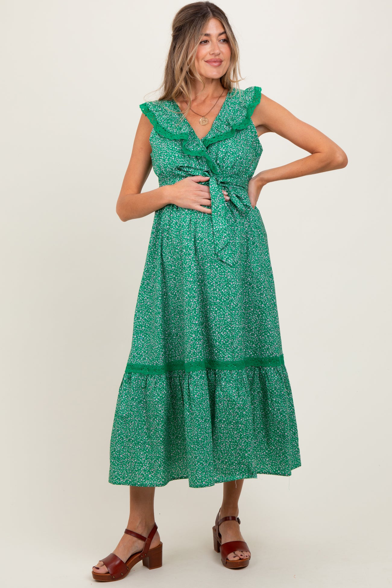 woman wearing a green floral maternity dress with ruffled straps and a tie waist, holding her baby bump