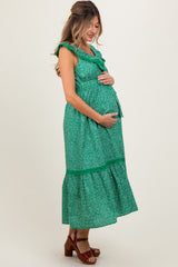 woman wearing a green floral maternity dress with ruffles and a tiered skirt, gently cradling her baby bump
