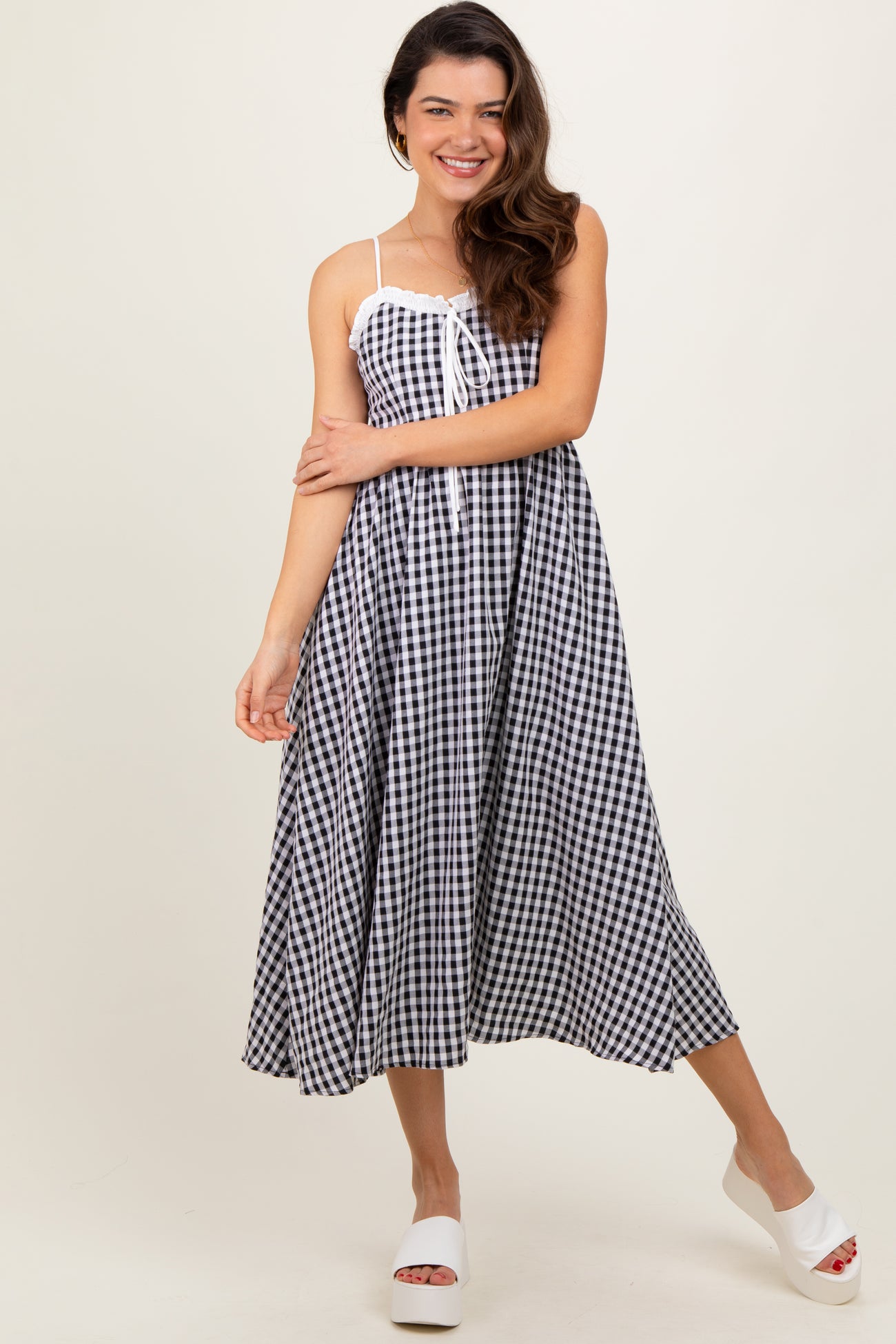 woman wearing a black and white gingham midi dress with adjustable straps and a tie detail at the bust