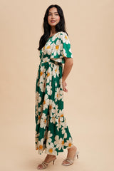 woman wearing a green floral maxi dress with short sleeves and a cinched waist, standing against a neutral background