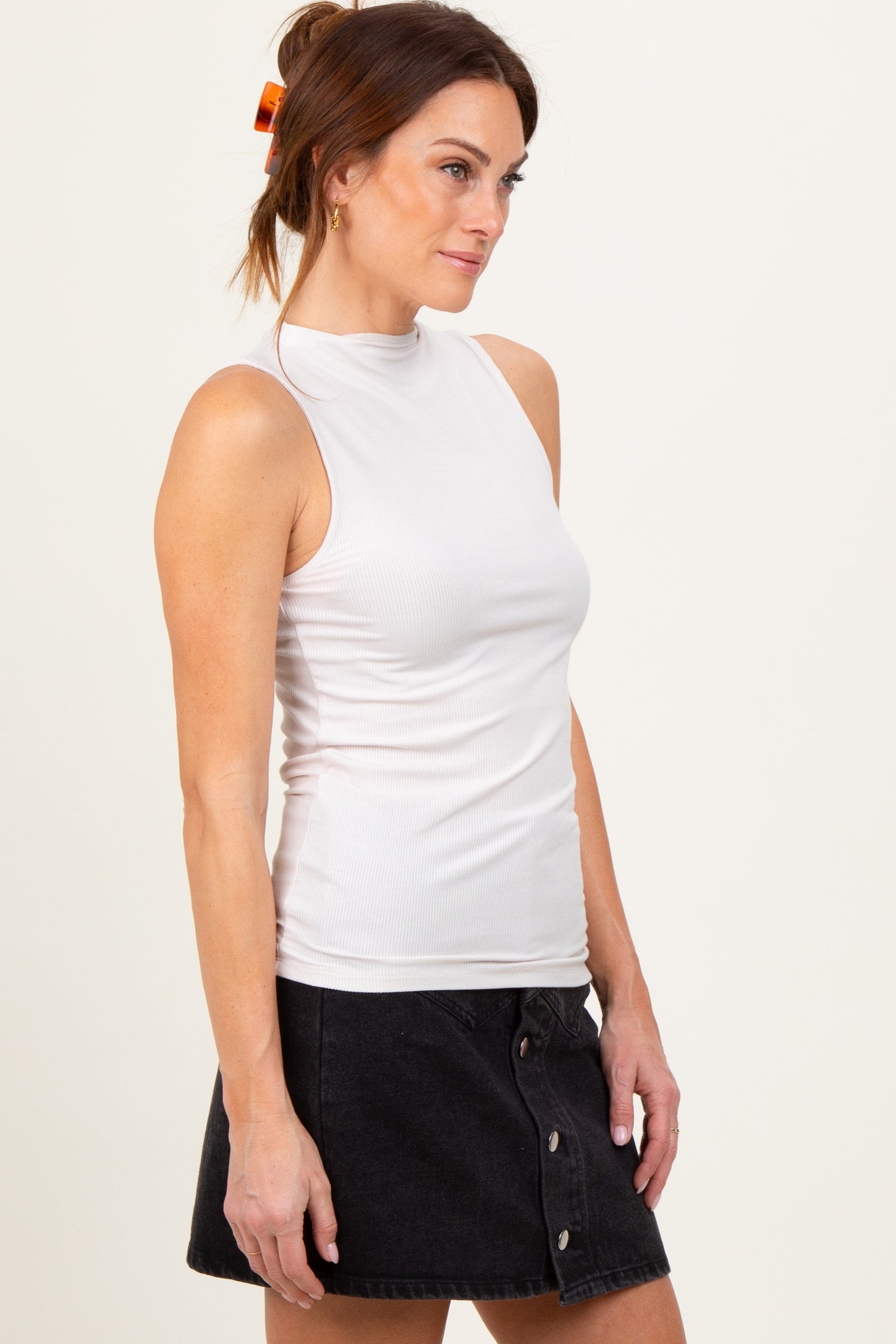 woman wearing a white sleeveless mock neck top paired with a black denim skirt