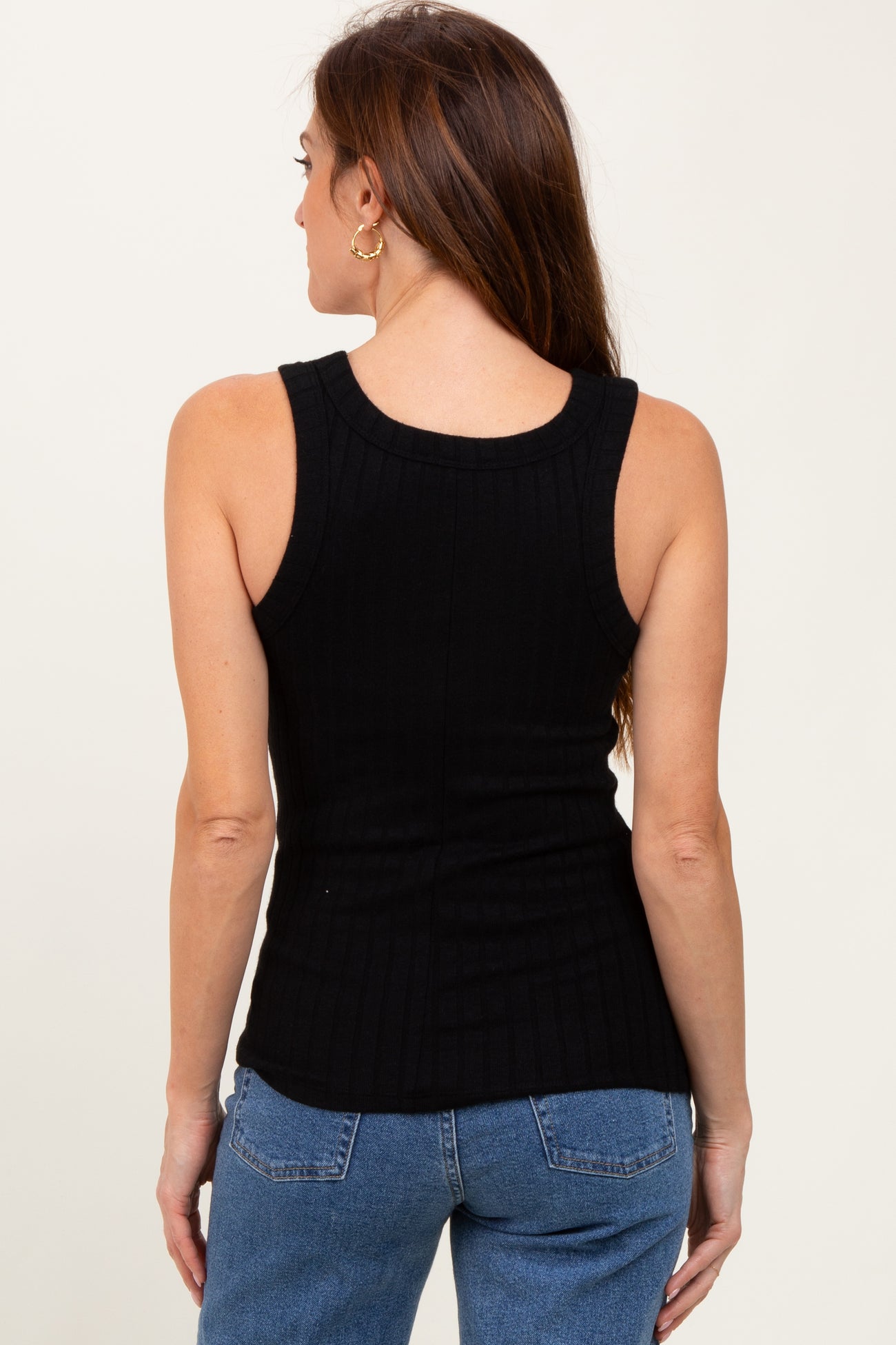 woman wearing a black ribbed tank top with a fitted silhouette and paired with blue jeans, viewed from the back