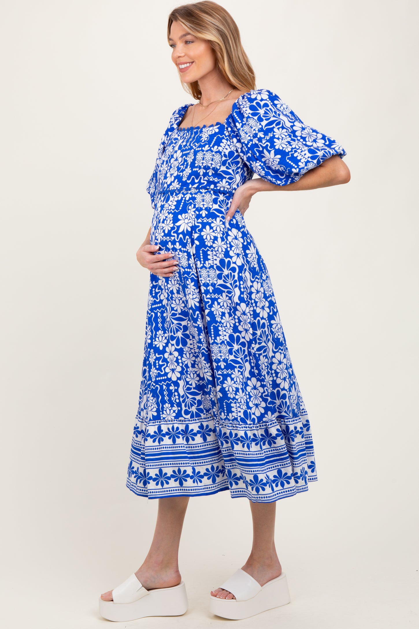 woman wearing a blue floral print maternity dress and gently cradling her baby bump