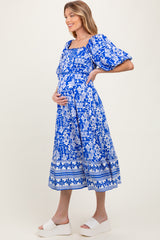 woman wearing a blue floral print maternity dress and gently cradling her baby bump
