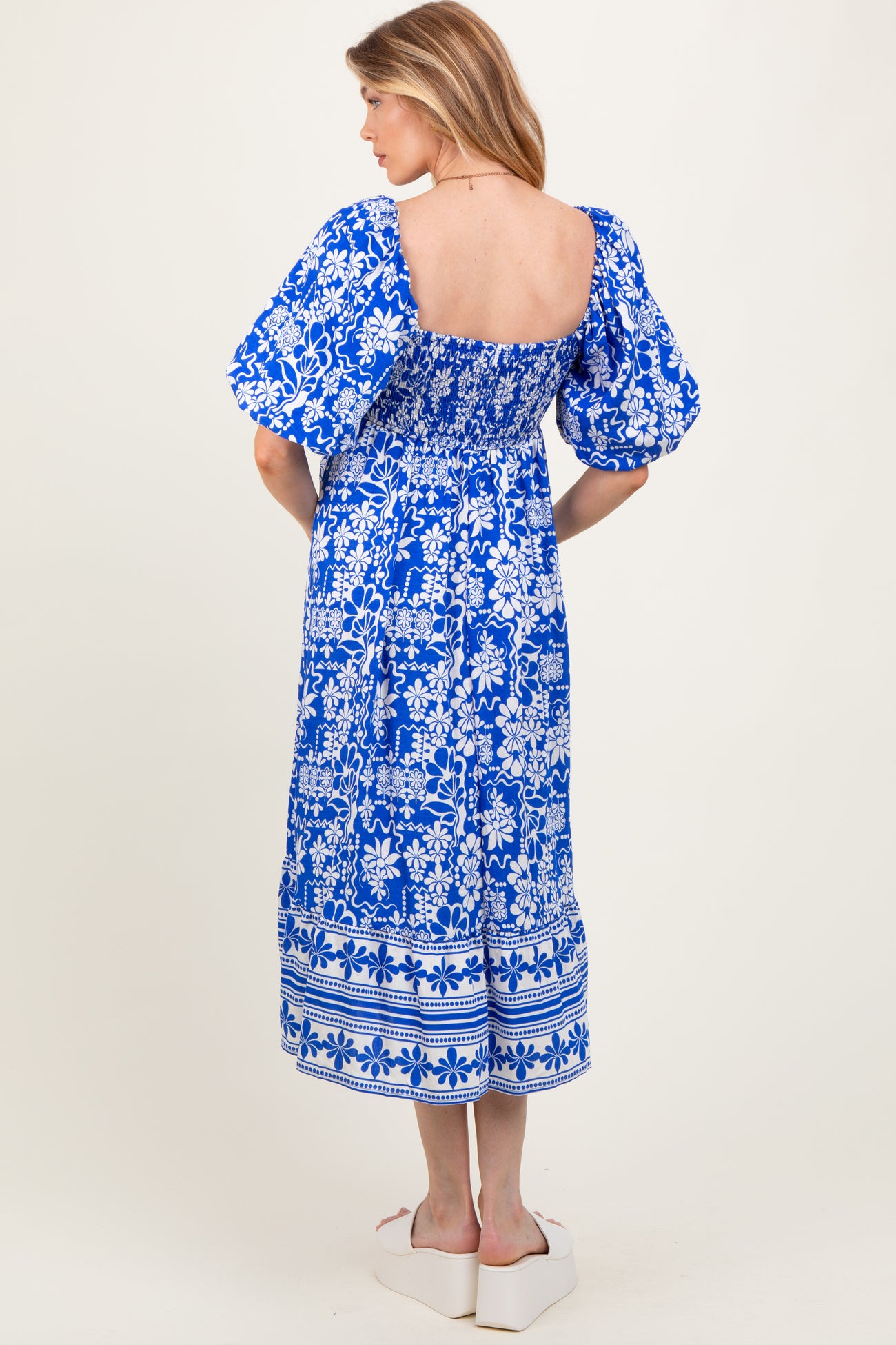 woman wearing a blue floral print maternity dress with puff sleeves and a smocked back, showing a baby bump