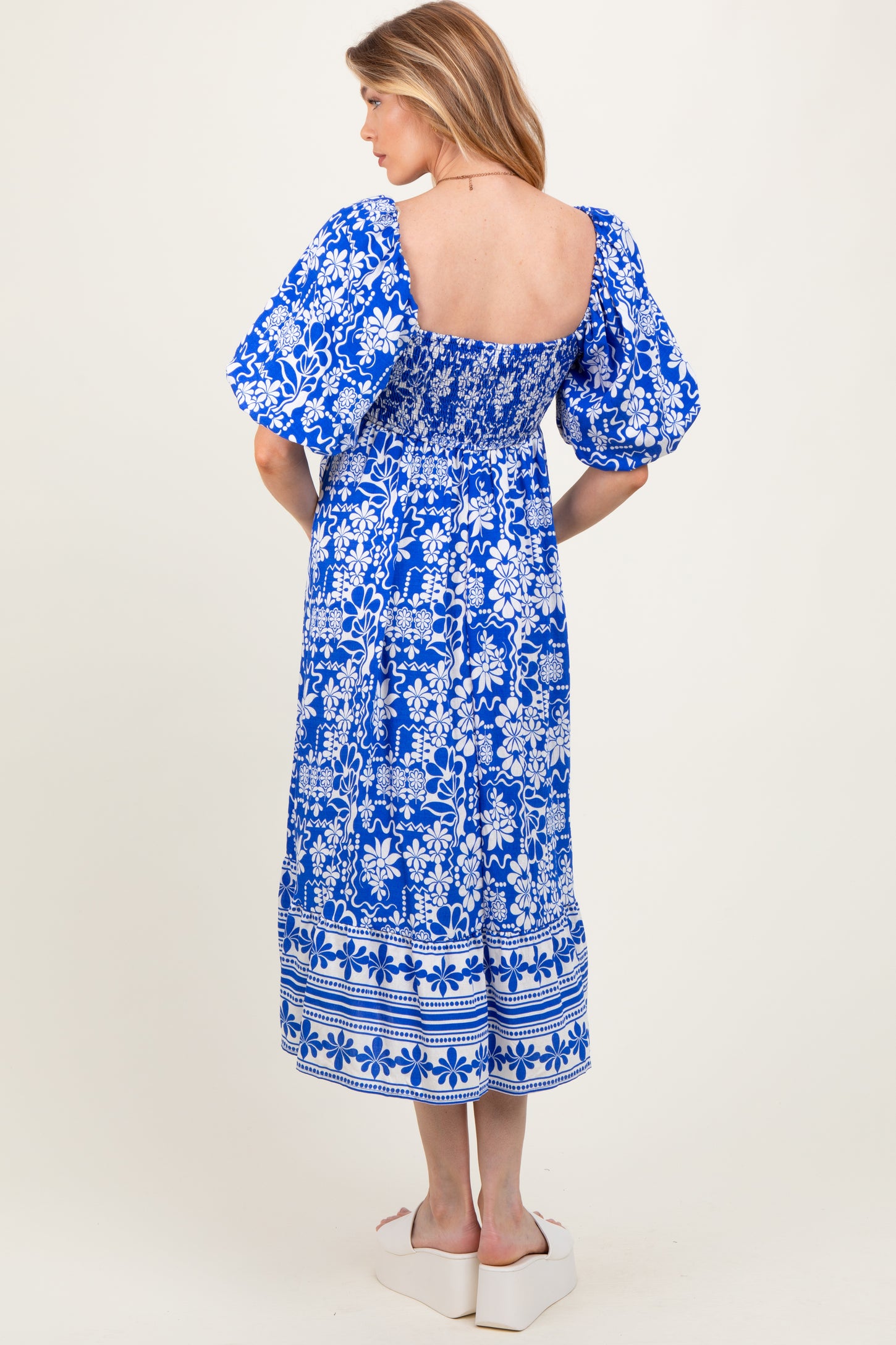 woman wearing a blue floral print maternity dress with puff sleeves and a smocked back, showing a baby bump